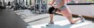 A woman kneels on the floor in the gym and stretches. She is wearing a knee support.