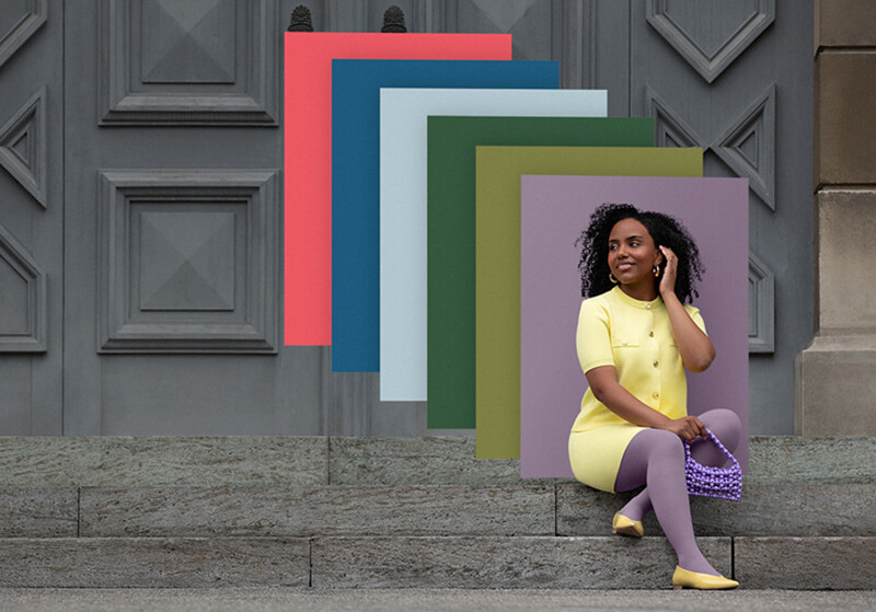 Une femme est assise sur des marches en pierre devant un portail. Elle porte un ensemble deux pièces jaune clair et un bandage compressif violet. Derrière elle, on aperçoit des aplats de couleurs tendance.