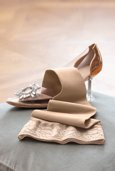 4. Lifestyle Bild Juzo Soft  Juzo Soft Sesam liegt auf einem Kissen neben einem Cinderella Schuh