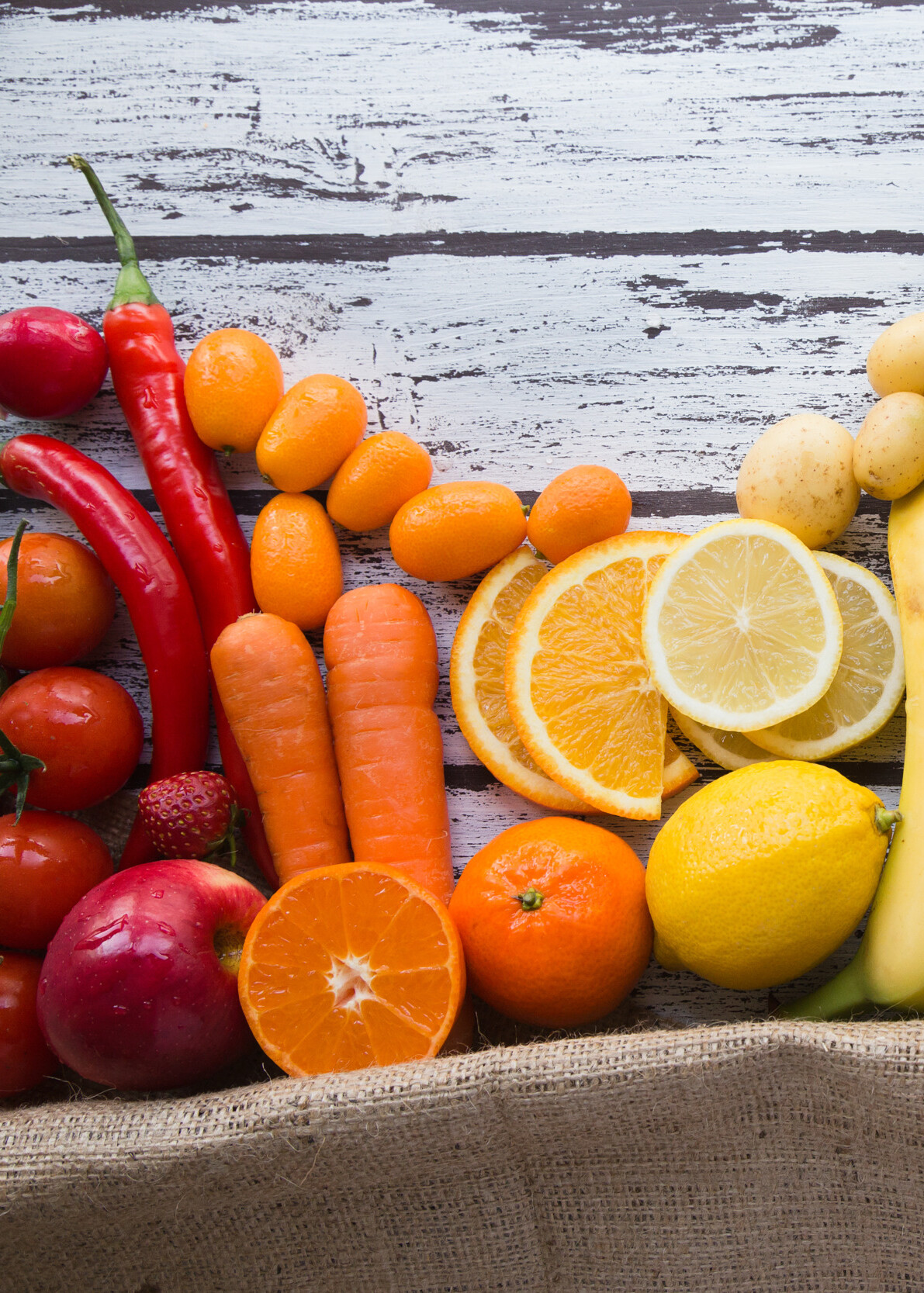 Die meisten Inhaltsstoffe kann man auch auf natürlichem Weg über spezielle Lebensmittel ohne Zusatzstoffe decken Auf einem holzigen Hintergrund erkennt man buntes Obst und Gemüse aufgereiht nebeneinander. Es bildet sich so ein Farbverlauf von rot, orange, gelb bis zu grün und rot