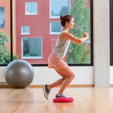 Exercise Single-leg squats Step 2 A woman standing on a soft cushion with one leg, doing a squat