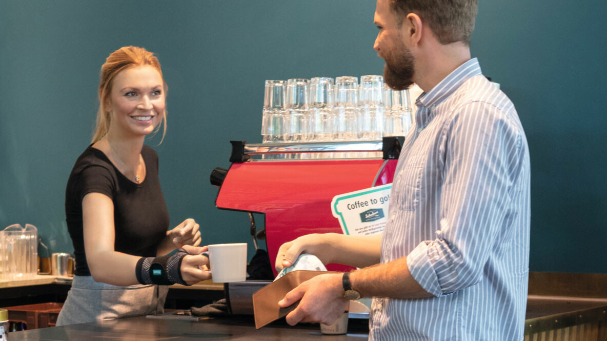 Hand pain A bakery shop assistant hands a customer a coffee cup. She is wearing a wrist bandage.