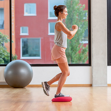 Exercise Single-leg squats Step 1 A woman standing on a soft cushion with one leg, slightly lifting the other leg