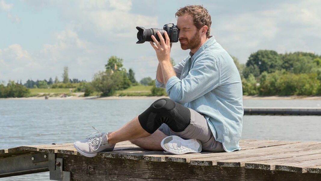 Knee pain A photographer sits on a jetty with his camera and takes pictures.