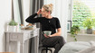 Una mujer con un vendaje de tórax negro está sentada en un tocador y tiene una taza de té en la mano