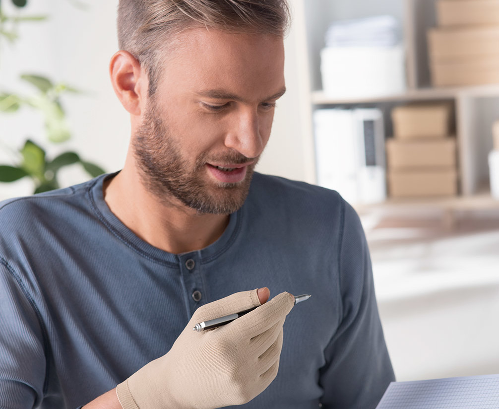 Juzo ScarPrime Seamless Handschuh Mann mit Juzo ScarPrime Seamless Handschuh hält Stift in der Hand