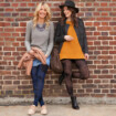 Zwei Frauen lehnen an einer Backsteinwand und tragen zu ihren Outfits Kompressionsstrumpfhosen von Juzo mit Batikmuster