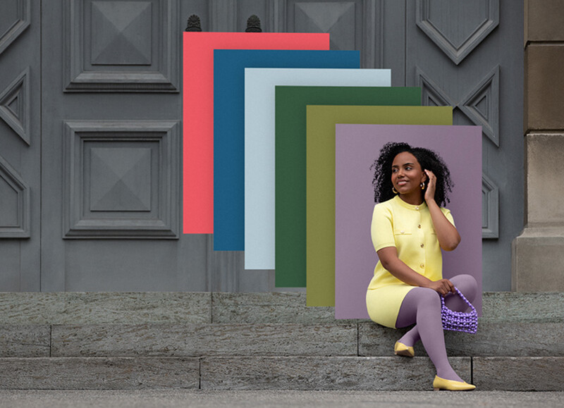 Trend Colours 2026 / 27 Eine Frau sitzt auf Steinstufen vor einem Tor. Sie trägt einen hellgelben Zweiteiler zu einer lilanen Kompressionsversorgung. Hinter ihr sieht man Farbfelder in den Trend Colours