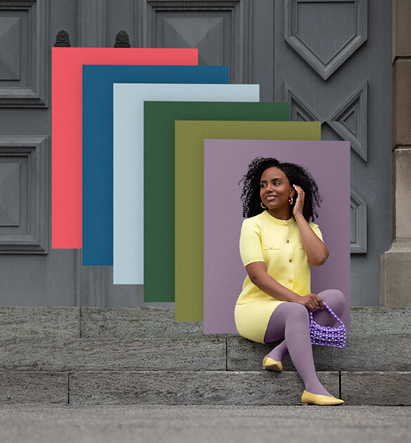 Juzo Trend Colours Batik Eine Frau sitzt auf Steinstufen vor einem Tor. Sie trägt einen hellgelben Zweiteiler zu einer lilanen Kompressionsversorgung. Hinter ihr sieht man Farbfelder in den Trend Colours